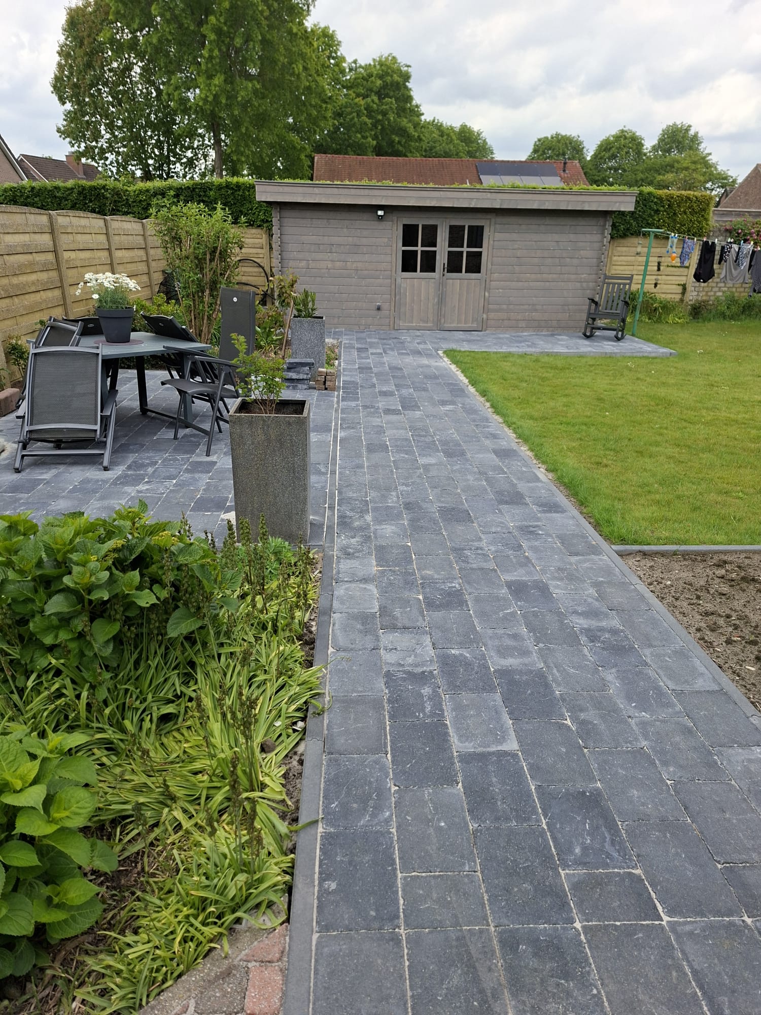 Aangelegd pad in blauwe kasseien naar tuinhuis met terras